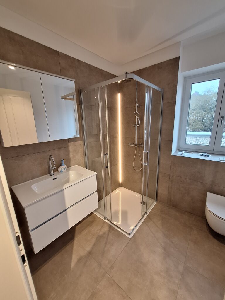 Fertiges Bad mit Glasdusche, großformatigen Wandfliesen und Waschtisch
