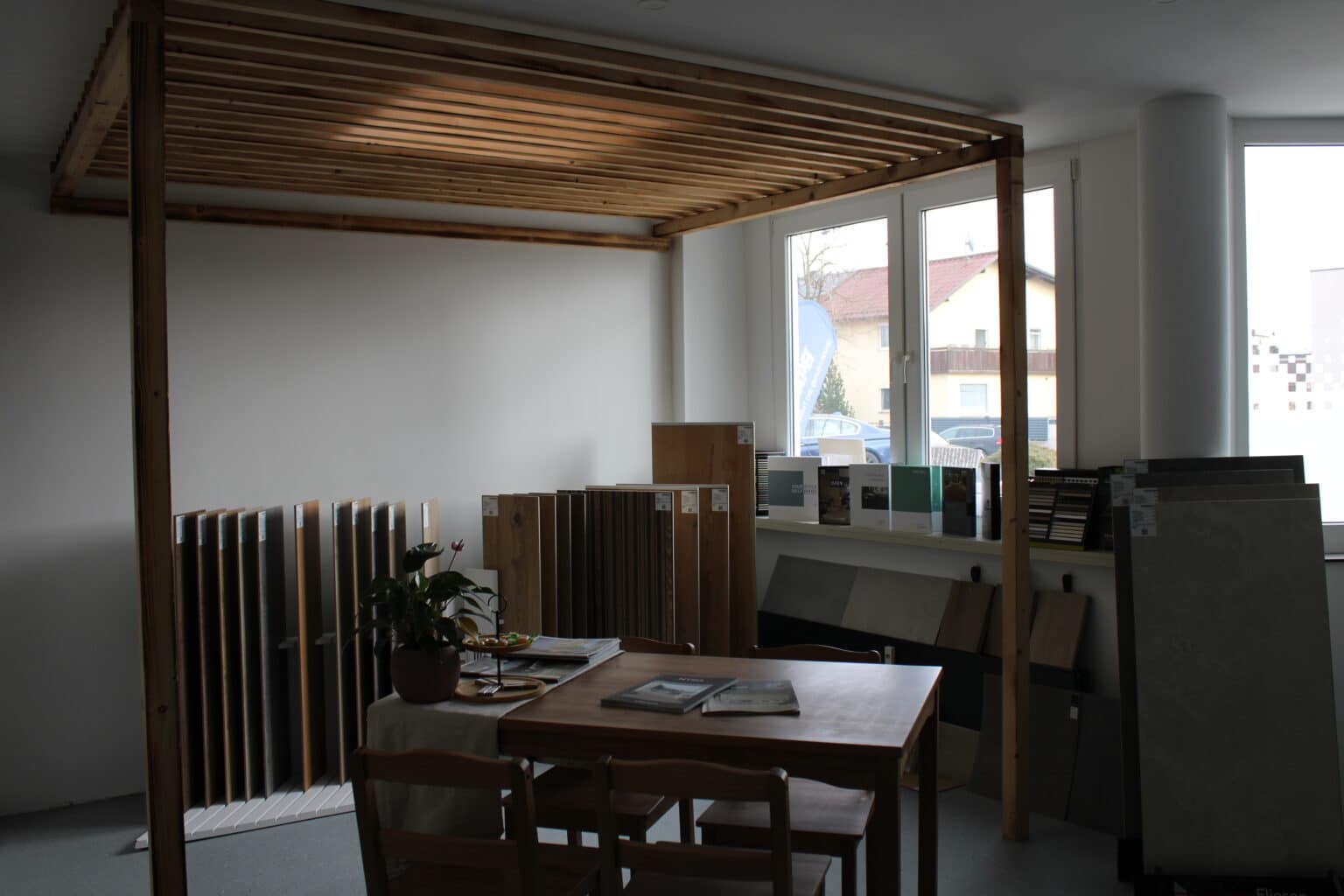 Beratungstisch im Schauraum unter einer Holzpergola, dahinter Musterplatten